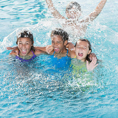 Multi-ethnic group of children (9 to 13 years) playing in swimming pool, splashing.